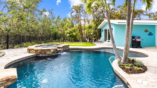 A swimming pool with a waterfall feature, surrounded by palm trees and a well-maintained lawn.