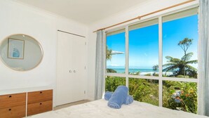 A bedroom with a large window, a bed, a wardrobe, and a mirror.