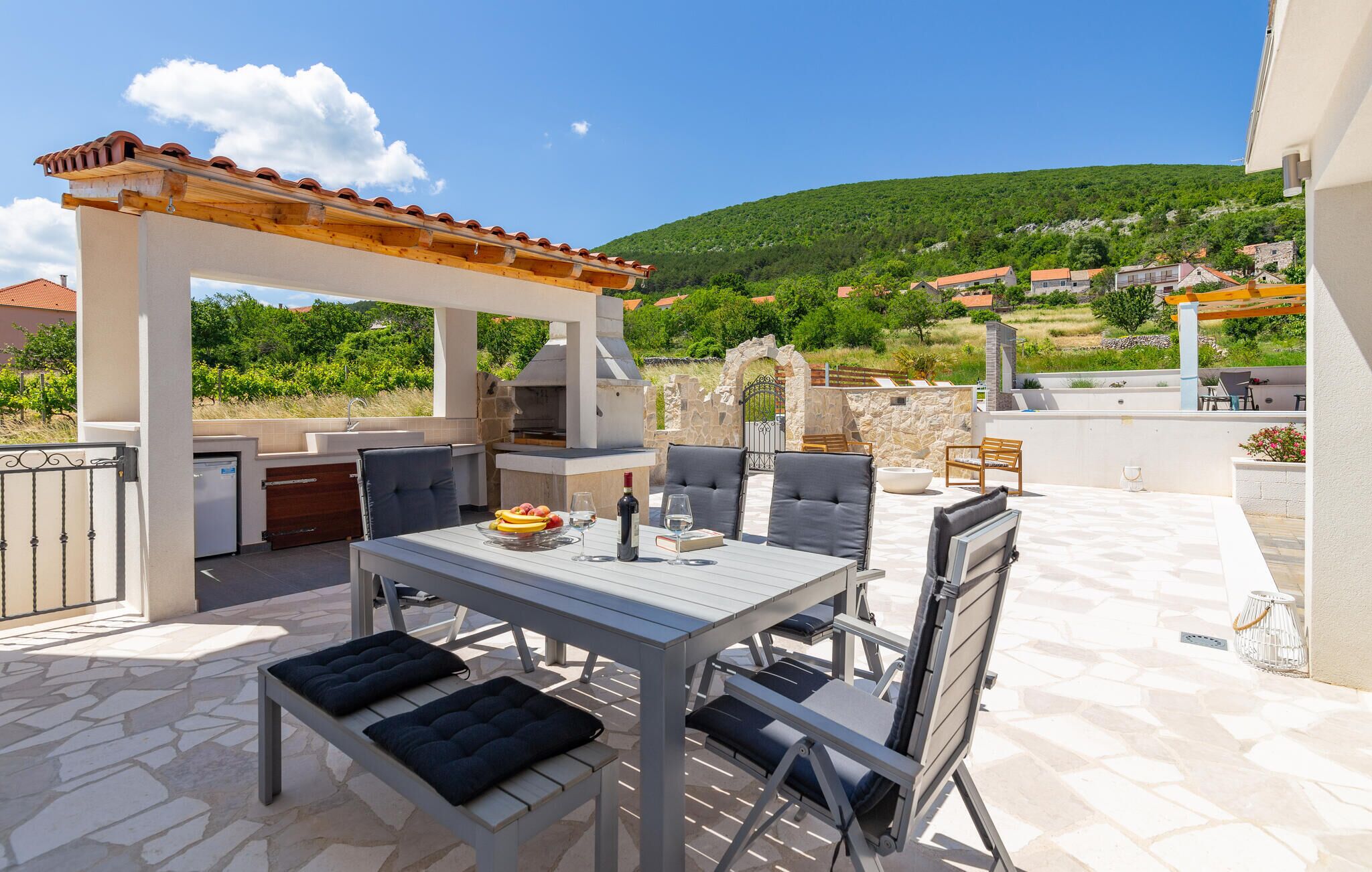 An outdoor patio with a table and chairs, a grill, and a view of a hillside.
