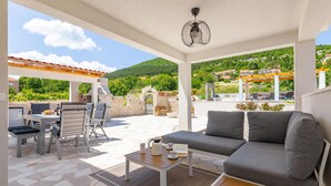 En uteplats med en soffa, ett matbord och stolar, en grill och en pergola.