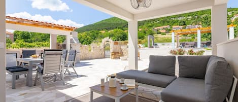 Eine Außenpatio mit einer Sitzecke, einem Esstisch, Stühlen, einem Grill und einer Pergola.