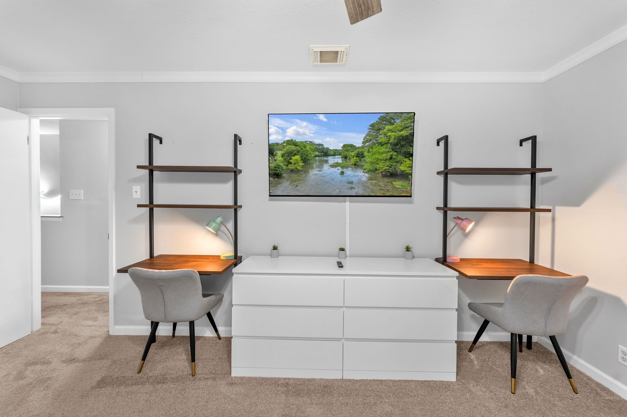 A modern room with a white desk, two chairs, a flat-screen TV, and built-in shelving.