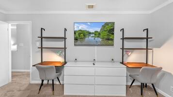 A modern room with a white desk, two chairs, a flat-screen TV, and built-in shelving.