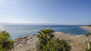 Blick auf die Küste mit einem felsigen Strand, blauem Meer und Bergen in der Ferne.