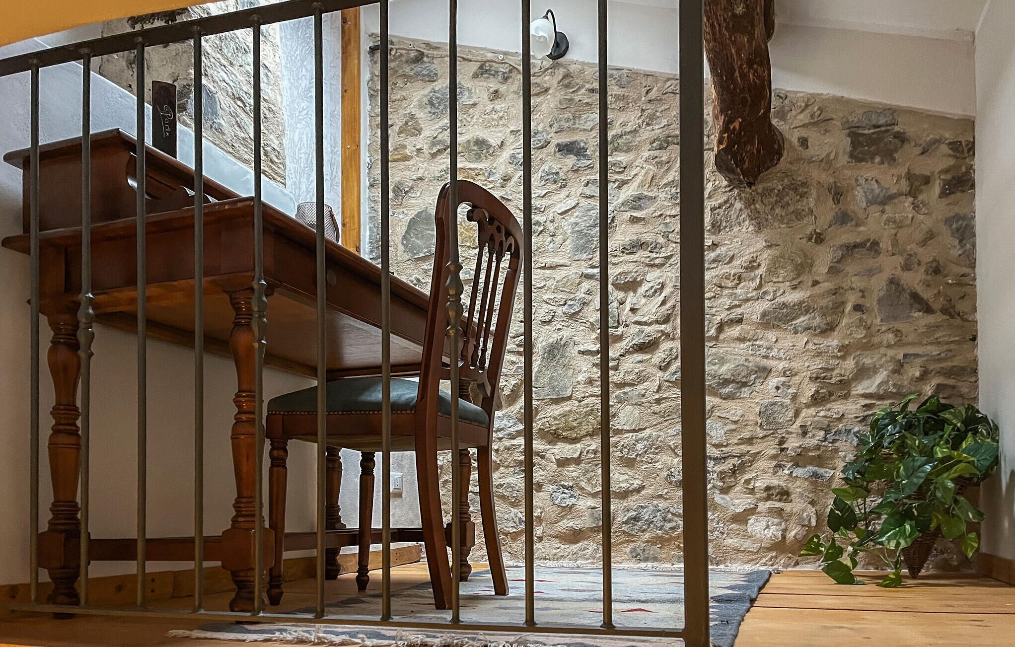 A staircase with a wooden railing, a stone wall, and a chair with a cushion.