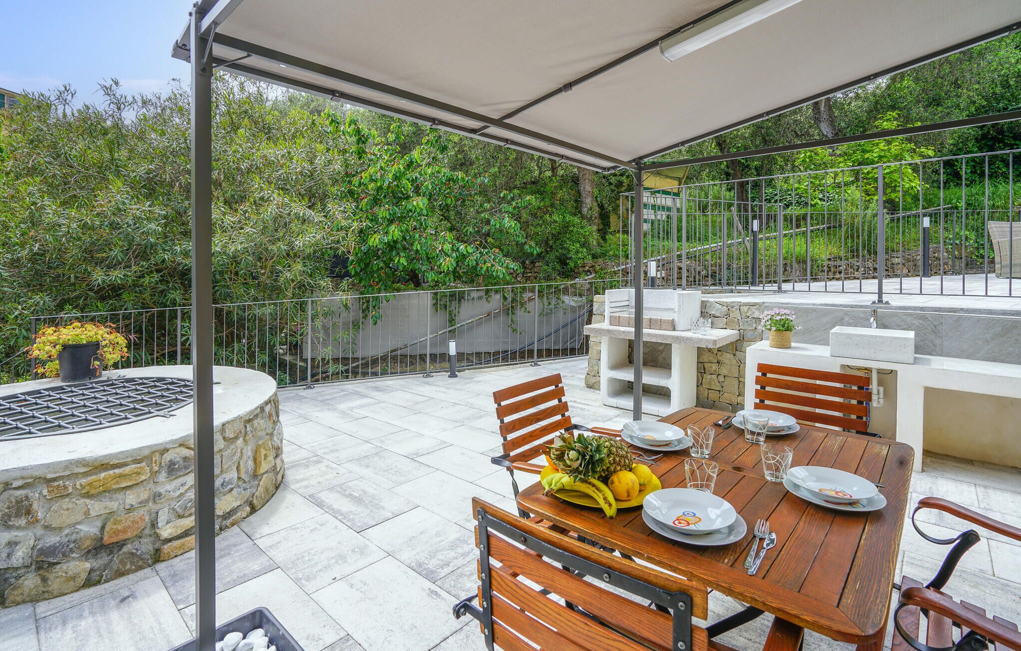 An outdoor patio with a table set for two, surrounded by stone walls and a metal fence.