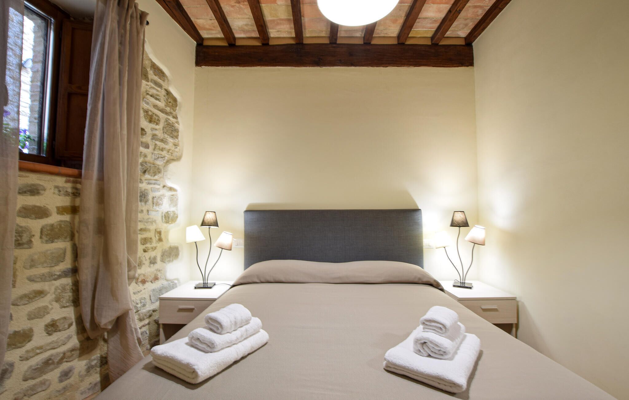Ein Schlafzimmer mit Steinwand, Holzboden und einem Bett mit zwei Nachttischen und zwei Lampen.