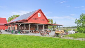Um edifício estilo celeiro vermelho chamado "LILJENÄS GÅRD" com área de estar ao ar livre e uma charrete puxada por cavalos.