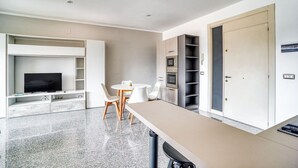 A modern hotel room with a flat-screen TV, a dining table with chairs, a kitchenette, and a wardrobe. - GuestHost - Casa Frida, apartement with balcony (Foligno)