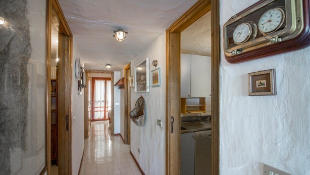 A hallway with a kitchen area, wooden doors, and a clock on the wall. - GuestHost - Dreamy Sea View with Pool and Parking (Olbia)