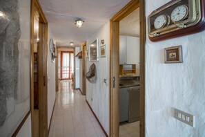 A hallway with a kitchen area, wooden doors, and a clock on the wall.