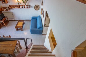 A staircase leading to a living area with a blue sofa, wooden furniture, and wall decorations. - GuestHost - Dreamy Sea View with Pool and Parking (Olbia)