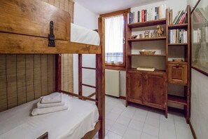 A bunk bed with a wooden headboard, a bookshelf with books and decorative items, and a window with curtains.