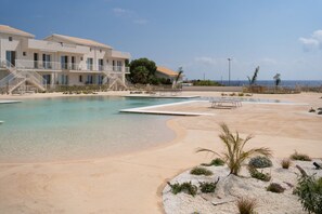 A resort with a swimming pool, a beach area, and a building with balconies.