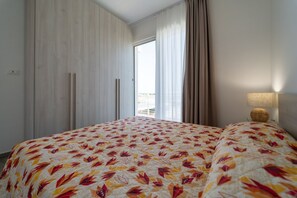 A hotel room with a large bed, a wardrobe, a window with curtains, and a lamp on the nightstand.
