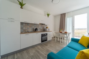 Una cocina moderna con armarios blancos, una encimera de madera y un salpicadero de azulejos. Hay un comedor con una mesa y sillas, y un sofá azul con almohadones amarillos.
