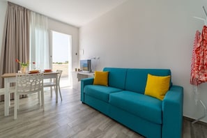 Una sala de estar moderna con un sofá azul verdoso, una mesa de comedor con sillas y vistas por un ventanal grande.