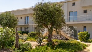 A multi-story building with balconies, a garden with various plants, and a staircase leading to the upper floors. - GuestHost - Cozy 40 sqm seaview flat, able to accommodate up to 3 people, located inside the renowned Borgo 84 residence, equipped with swimming pool and cycle path. The property is located just 3 km from the center of Marzamemi, one of the most fascinat (Pachino)