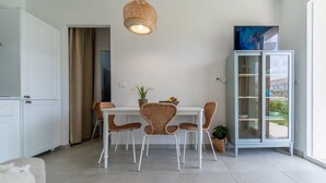 A modern kitchen with white cabinetry, a dining table with wicker chairs, a hanging light fixture, and a glass cabinet with a view. - GuestHost - Cozy 40 sqm seaview flat, able to accommodate up to 3 people, located inside the renowned Borgo 84 residence, equipped with swimming pool and cycle path. The property is located just 3 km from the center of Marzamemi, one of the most fascinat (Pachino)