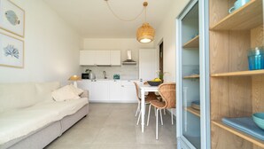 A modern kitchen with white cabinets, a dining area with wicker chairs, and a glass door leading to a balcony. - GuestHost - Cozy 40 sqm seaview flat, able to accommodate up to 3 people, located inside the renowned Borgo 84 residence, equipped with swimming pool and cycle path. The property is located just 3 km from the center of Marzamemi, one of the most fascinat (Pachino)
