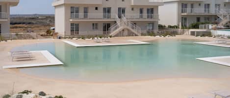 Zona de piscina con cielo despejado, un edificio con varios balcones y una escalera que lleva al piso superior.