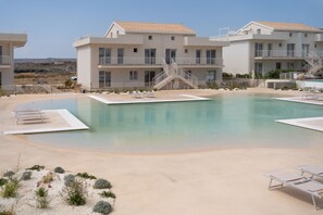 Une piscine entourée d’un espace où le ciel est dégagé, un bâtiment doté de nombreux balcons et un escalier menant à l’étage supérieur.