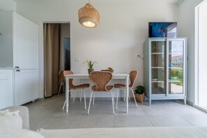 Una cocina moderna con armarios blancos, una mesa de comedor con sillas de mimbre, una lámpara colgante y un aparador de vidrio con vistas.