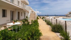 A hotel with a pool, outdoor seating, and a staircase leading to the upper floors. - GuestHost - Cozy 40 sqm seaview flat, able to accommodate up to 3 people, located inside the renowned Borgo 84 residence, equipped with swimming pool and cycle path. The property is located just 3 km from the center of Marzamemi, one of the most fascinat (Pachino)