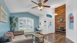 A living room with a ceiling fan, a sofa, a coffee table, and a window with blinds.