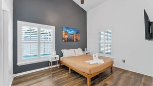 A bedroom with a bed, two windows with blinds, a ceiling fan, and a painting on the wall.