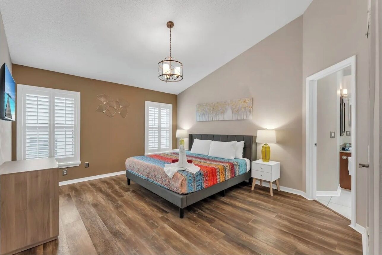 A bedroom with a large bed, a bedside table with a lamp, a wall-mounted artwork, and a ceiling light fixture.