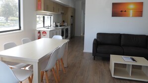 A modern kitchen with white cabinets, a dining area with a white table and chairs, a black sofa, and a painting of a sunset. - BIG4 Kingston Foreshore Holiday Park (Kingston SE)