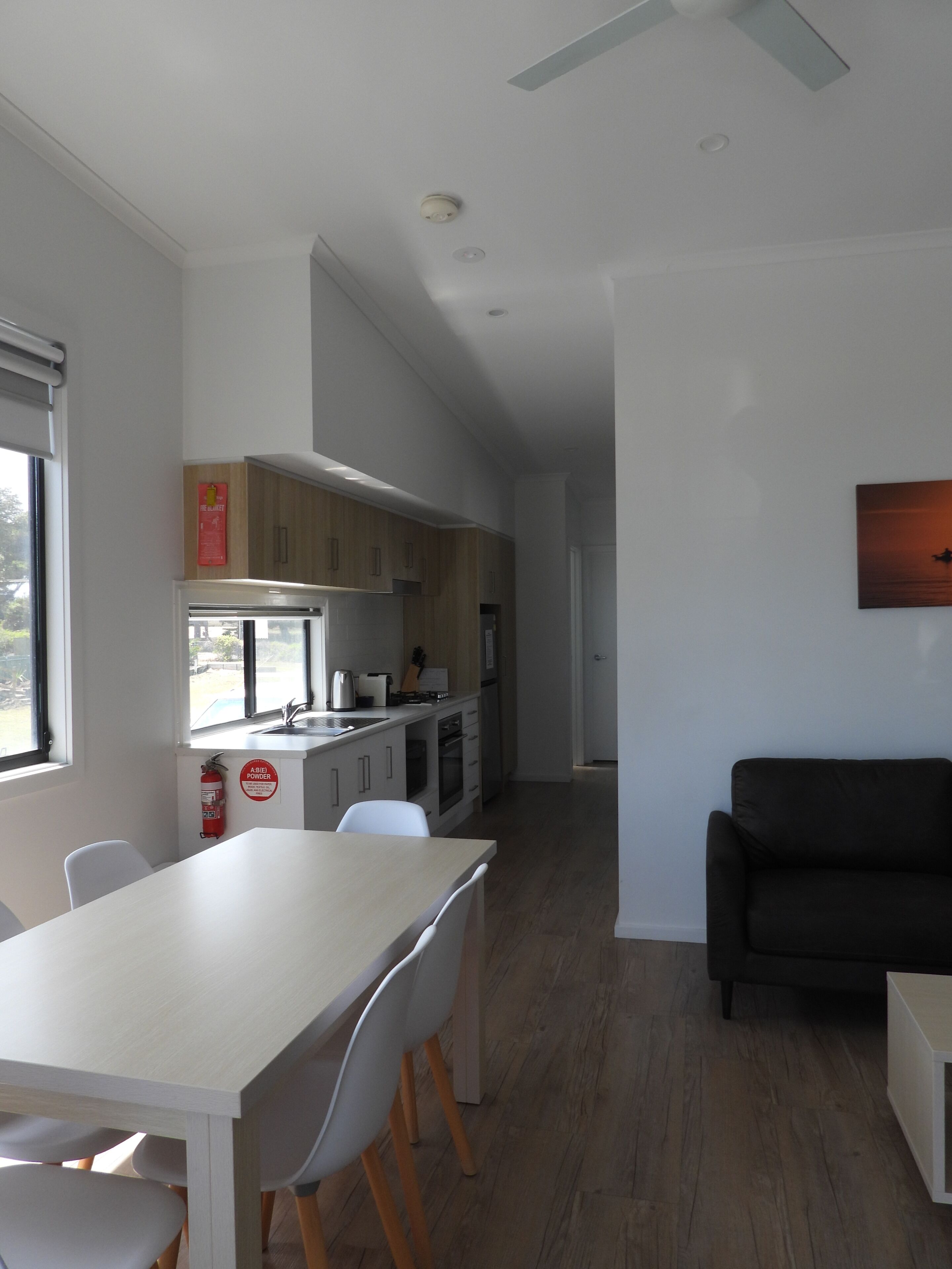 A modern kitchen with wooden cabinets, a dining area with a white table and chairs, and a black sofa.