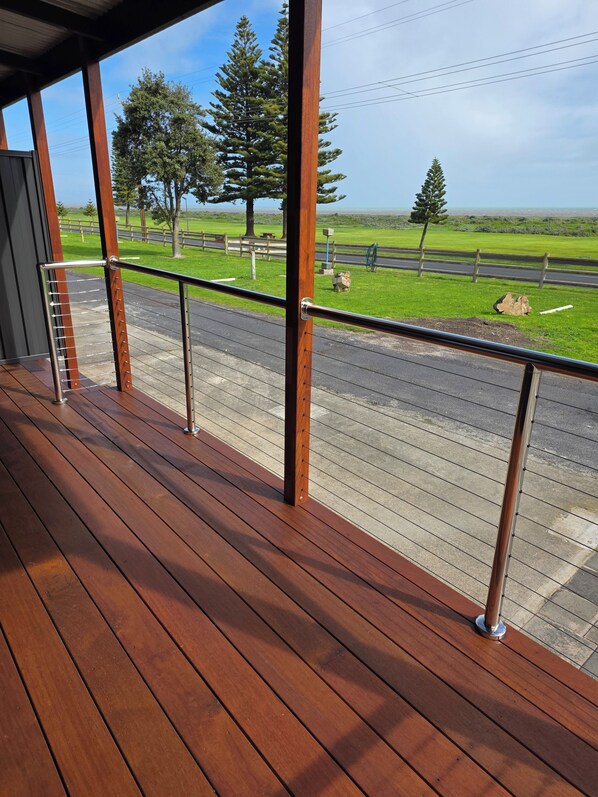 A wooden deck with a metal railing overlooking a road and green landscape.