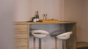 A bar area with a wooden counter, two white bar stools, a bottle of champagne, and a small decorative plant.