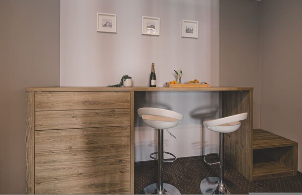 A bar area with wooden cabinets, two white bar stools, a bottle of champagne, and a fruit bowl. - Dream 19B Stylowe Studio Centrum Pralka (Bydgoszcz)