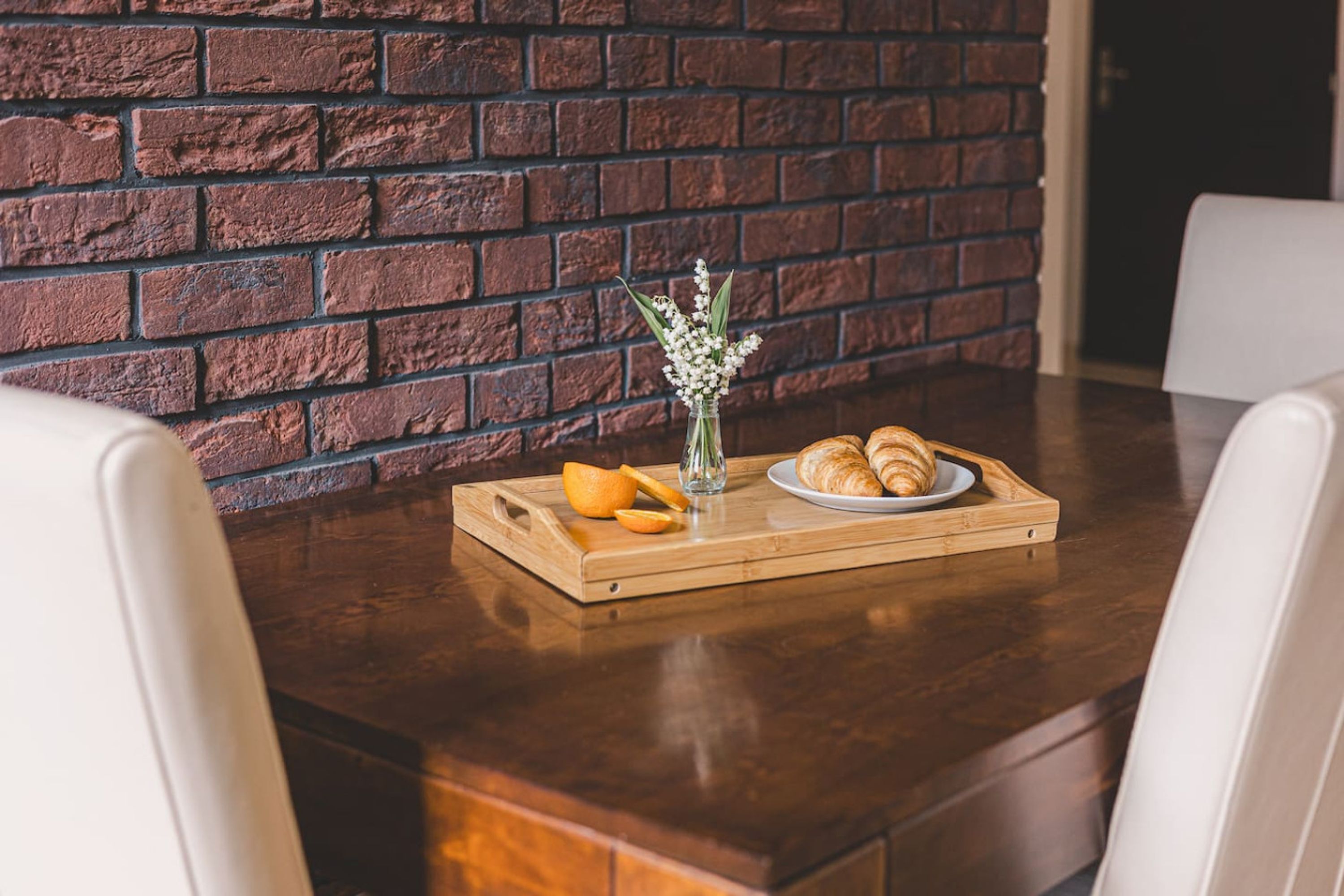 A dining table with a tray of croissants, a glass of white flowers, and an orange half.