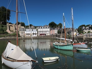 Ein Hafen mit mehreren vor Anker liegenden Booten, einer Steinmauer und Gebäuden im Hintergrund.
