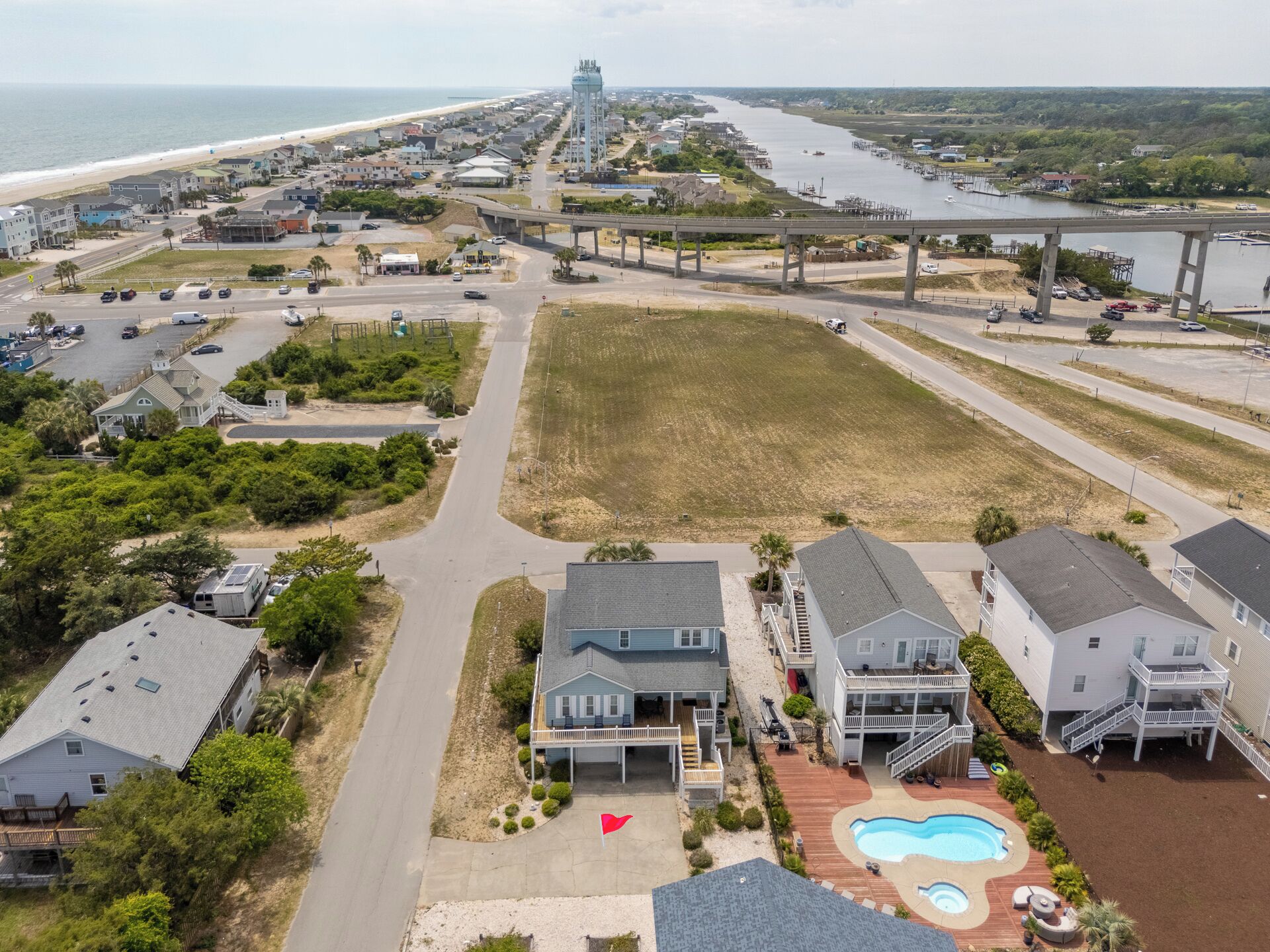 A coastal residential area with houses, a swimming pool, and a beach in the background.