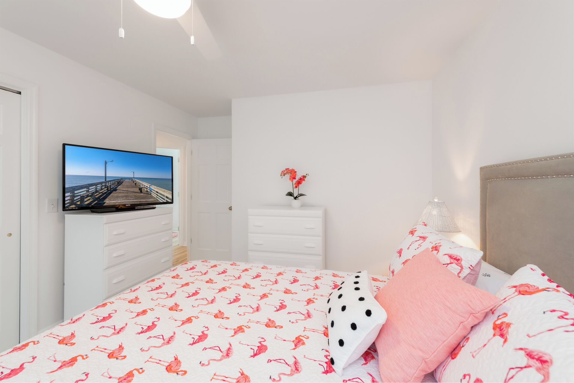 Ein Schlafzimmer mit einem Bett, einem Fernseher auf einer Kommode, einem Nachttisch mit Lampe und einer Tür zu einem weiteren Raum.