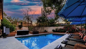 Une piscine entourée d’arbres, avec des chaises longues et des parasols, offrant une vue imprenable sur le coucher du soleil.