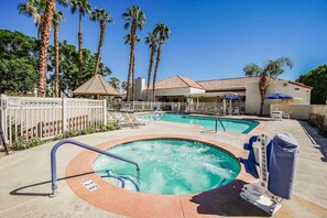 Un área de piscina de hotel con jacuzzi, sillas de descanso y palmeras.