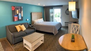 A hotel room with a bed, a sofa, a coffee table, a TV, and a painting on the wall.
