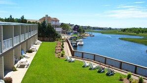 A hotel with a grassy terrace overlooking a river, lounge chairs, and a view of the water.