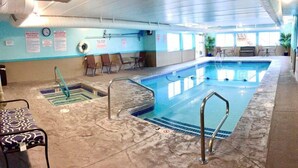 An indoor swimming pool with a tiled floor, a lifeguard chair, and a seating area with tables and chairs.