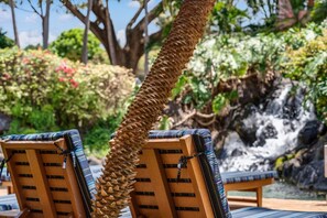 Two lounge chairs with striped cushions, a rope barrier, and a waterfall in the background. - Studio w/ Balcony & Full Kitchen | Access to Pool (Lahaina)