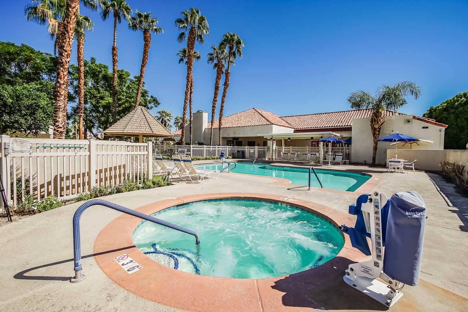 A hotel pool area with a hot tub, lounge chairs, and palm trees.