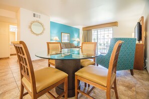 Un comedor con una mesa de vidrio rodeada de sillas de madera, una pared azul y una ventana con cortinas.