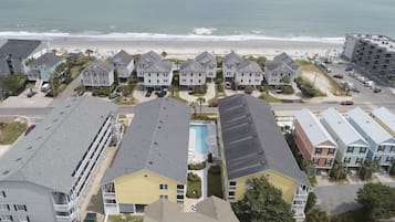 A beachfront residential area with multiple-story buildings, a visible swimming pool, and a beach in the background.