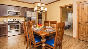 A dining area with a wooden table, chairs, and a chandelier. There is a kitchen with appliances like a microwave, oven, and refrigerator.